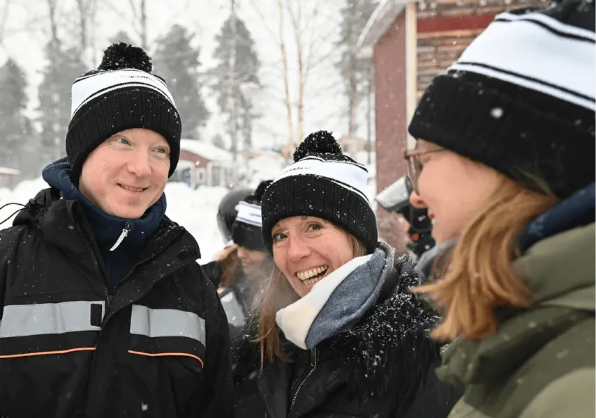 Three employees smile and wear black and white Stegra bobble hats surrounded by snow