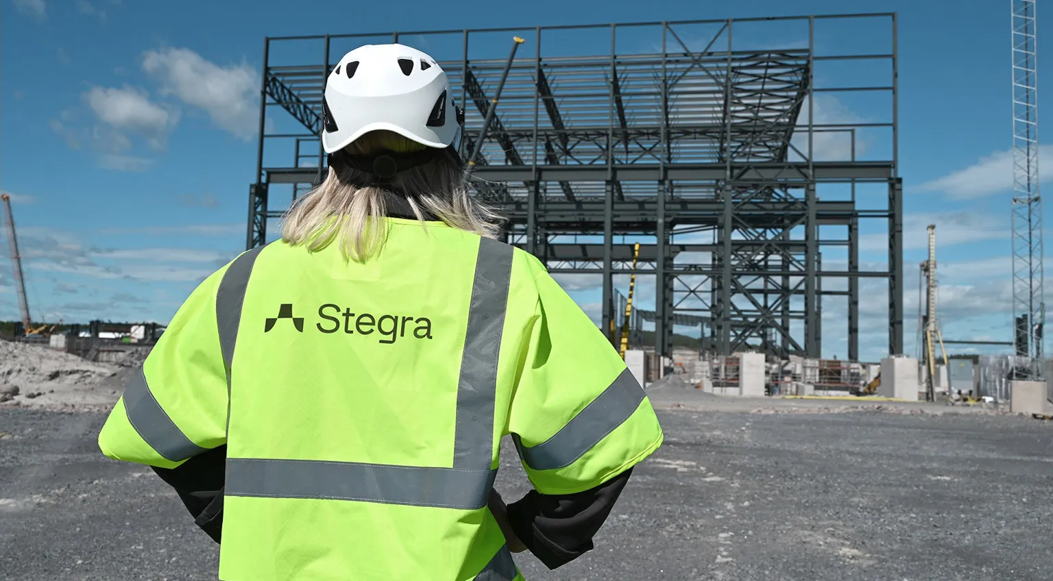 A woman in high-vis and hard hat looking at a steel frame