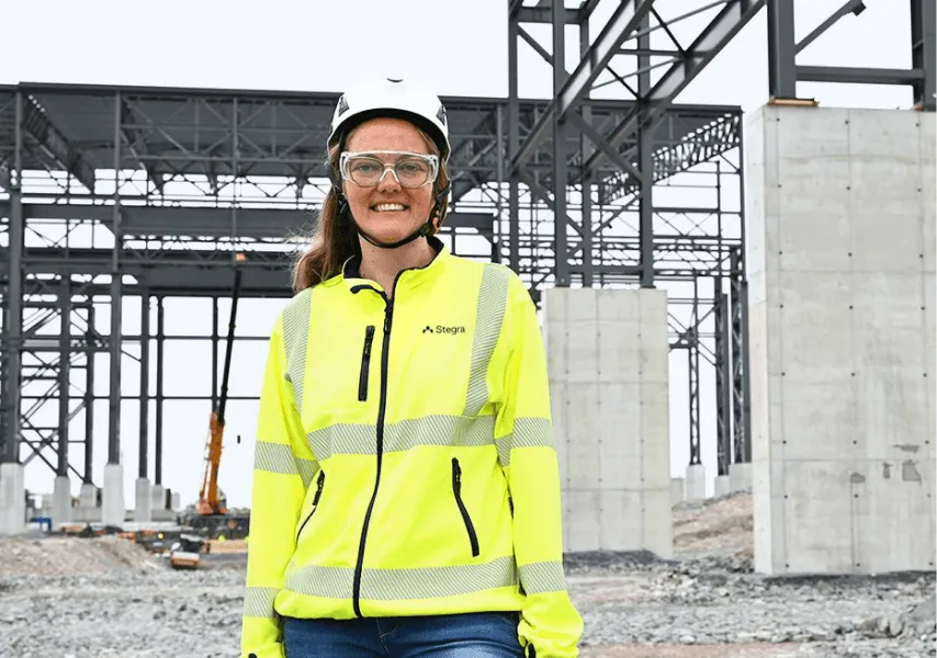 A female Stegra employee wearing safety gear smiles on-site 