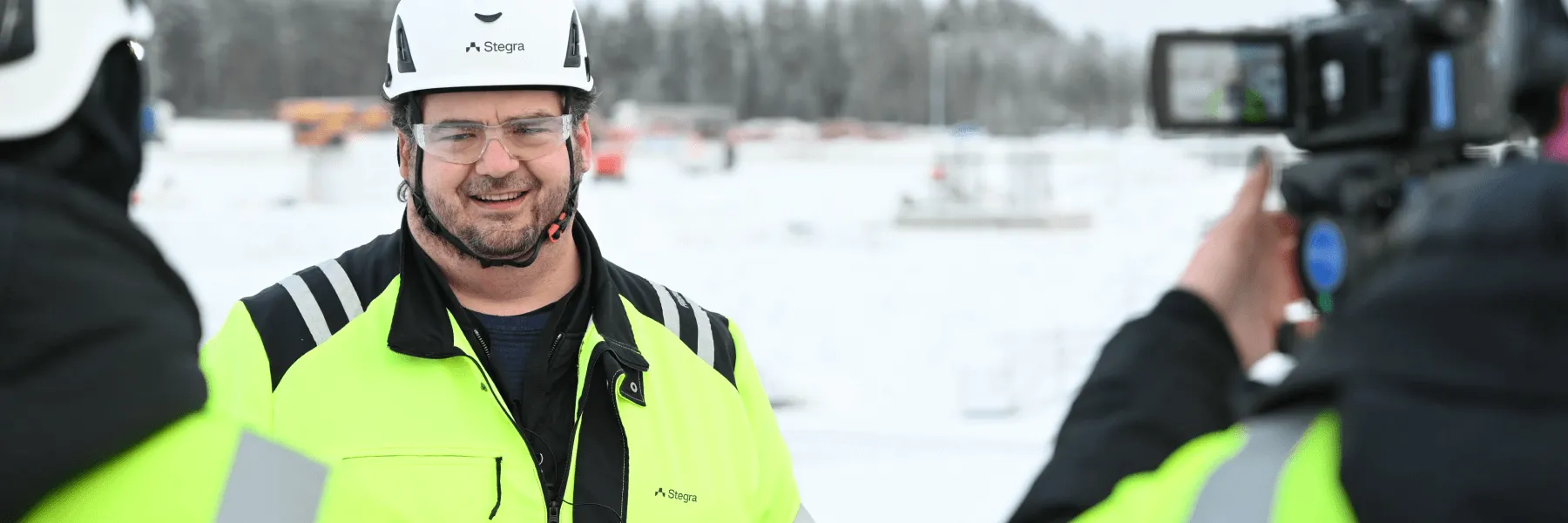 Employees in safety gear stand in the snow being filmed