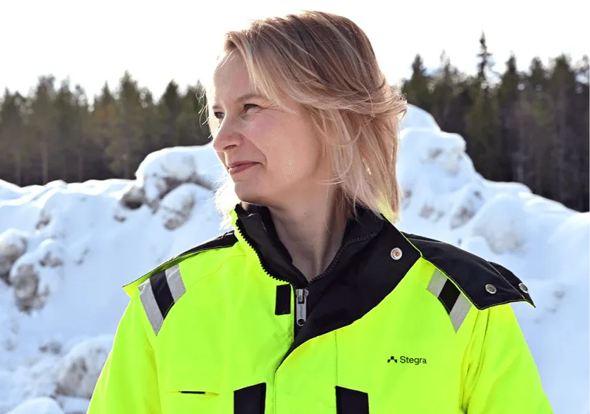 A woman stand outside in the snow with woodland in the distant background