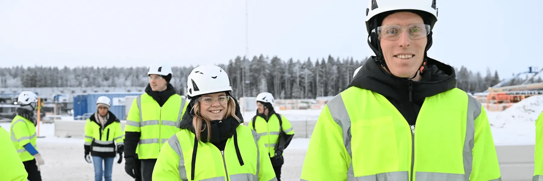 Multiple workers in safety gear and high-vis jackets walk through the snow