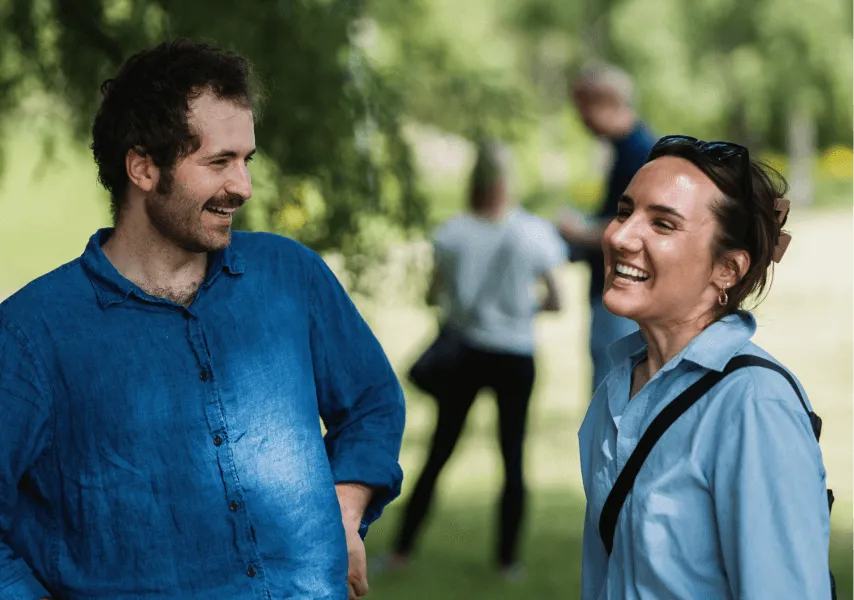 A man and a woman laugh in a sunny green field 